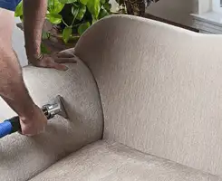 Professional upholstery cleaner deep-cleaning a fabric sofa with a handheld extraction tool and hose in Nashua, NH.